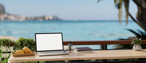 A remote workplace with a laptop mockup on a table on a balcony with a beautiful ocean sea view.