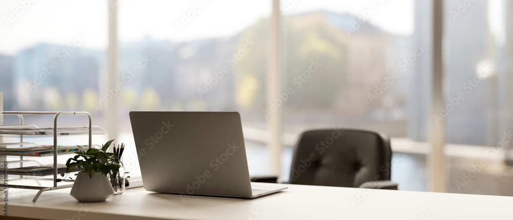 Poster back view image of a modern minimal bright office with a laptop computer on a white desk.