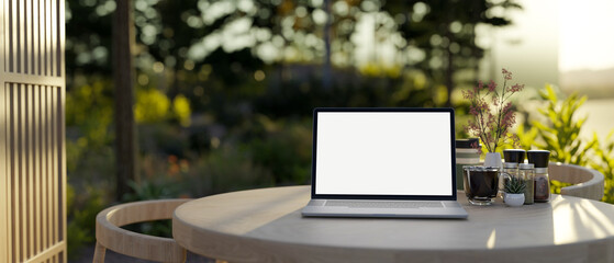 A laptop computer mockup on a wooden table on an outdoor patio lounge with a green garden.