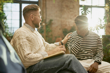 Side view portrait of bearded male psychologist supporting client during therapy session with lens...