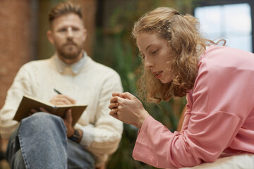 Fototapeta premium Side view portrait of struggling young woman sharing mental health problems with psychologist in therapy session, copy space