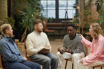 Diverse group of people sitting in circle during support group session with Black young man sharing...