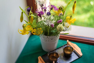 Bouquet of field yellow lilies and lilac, white cornflowers in a white pot on the windowsill