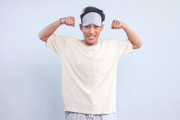 Excited young guy wear eye mask showing strong hands bicep muscle isolated over light blue background