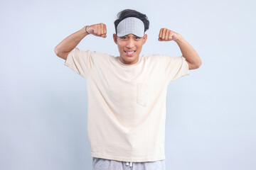 Naklejka premium Excited young guy wear eye mask showing strong hands bicep muscle isolated over light blue background