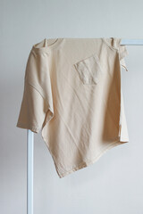 Plain beige t-shirt with pocket placed on steel bar of rack clothes