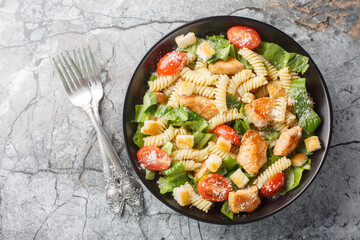 Tasty Caesar salad with pasta fusilli and other classic ingredients closeup on the bowl on the marble table. Horizontal top view from above