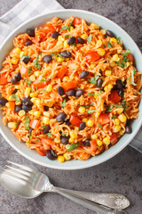 Mexican tomato rice with black beans, onions and corn close-up in a bowl on the table. Vertical top view from above