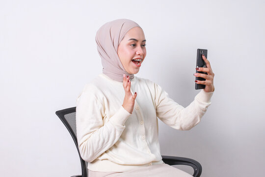 Young muslim girl with hijab and braces waving hand doing video call on smartphone while sitting