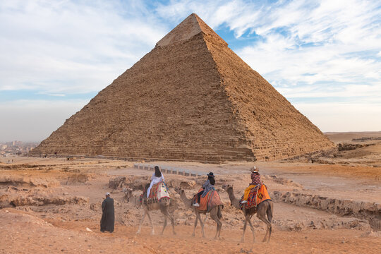 Group of tourists riding camels seeing the pyramids of Menkaure, Chephren and Cheops.