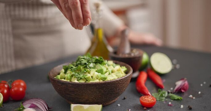 Salsa recipe - Woman salting Chopped ingredients in s wooden bowl - avocado, onion, cilantro and pepper