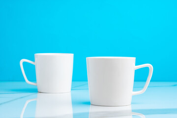 Two ceramic mugs on blue studio background