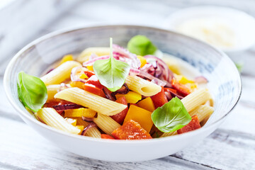 Penne pasta with yellow and red pepper, hard cheese and fresh basil. Bright background. Close up.