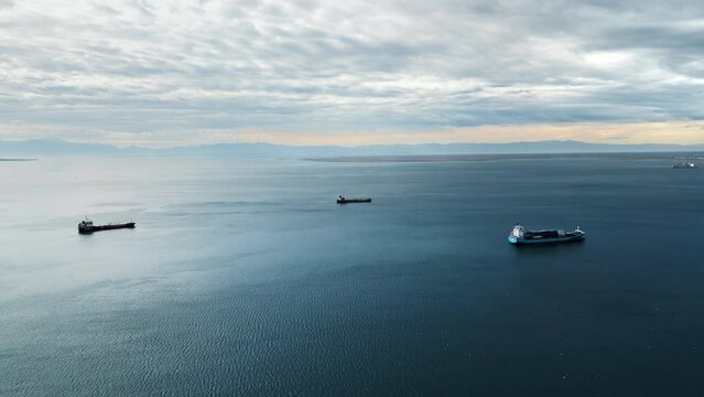 Aerial drone view of cargo ships floating in the middle of a large body of water. Clear sky, calm blue water