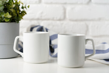 Two mugs on white table against brick wall background