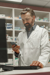Naklejka na ściany i meble Male pharmacist using the computer and phone while working at the pharmacy