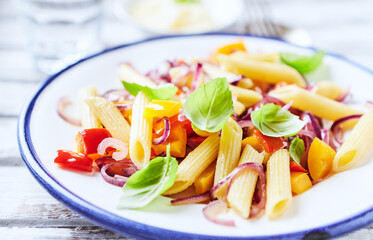 Penne pasta with yellow and red pepper, hard cheese and fresh basil. Bright background. Close up.
