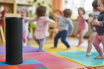speaker on a colorful mat, blurry toddlers wiggling to nursery rhymes