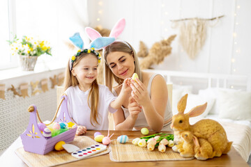 easter, a mother with a little daughter with hare ears on her head are preparing for the holiday by coloring colorful eggs, lifestyle, preparing a happy family with a child for Easter