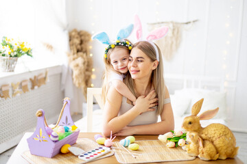 Obraz na płótnie Canvas easter, a mother with a little daughter with hare ears on her head are preparing for the holiday by gently hugging and kissing and spending time together, colorful eggs, lifestyle,