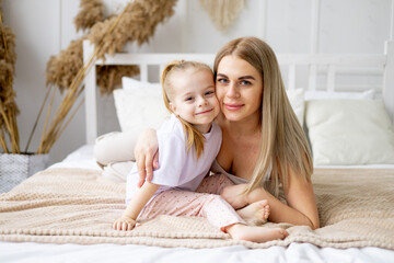 Obraz na płótnie Canvas mom and daughter play, hug and kiss at home on the bed, lifestyle, tender relationship of a young mother and child, happy family and motherhood