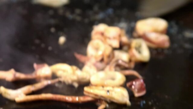 The process of cooking squid while stirring and adding sweet soy sauce looks close (Cumi)