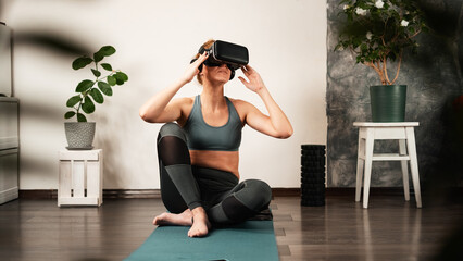 A young woman does yoga at home in a virtual reality helmet.