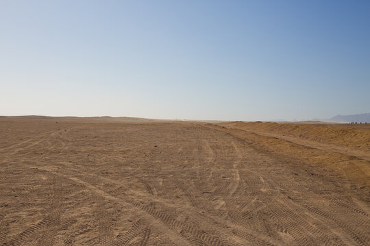 Desert road for buggy and ATV with tire tracks on the sand against the backdrop of the endless Arabian desert and clear sky