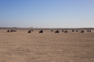 Obraz premium Group of tourists on ATVs during an excursion through the Arabian desert in Egypt. Extreme holiday in the desert on hot day