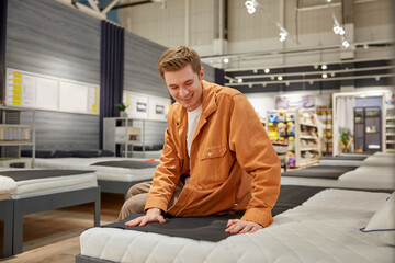 Handsome male customer sitting on new bed at furniture store