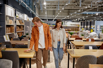 Positive loving couple testing new furniture for dining room at store - Powered by Adobe