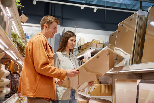 Happy loving couple choosing wall picture for home decoration at store