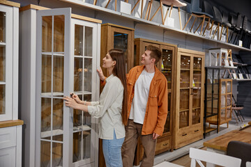 Young man and woman couple choosing cupboard at store market - obrazy, fototapety, plakaty