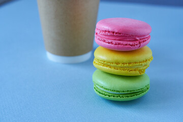 Colorful macaroons and paper coffee cup on blue background.