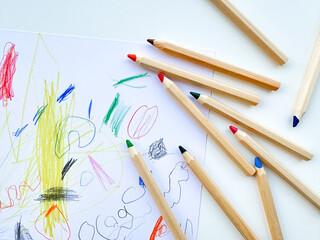 Colored pencils on the background of childs drawing. Top view.