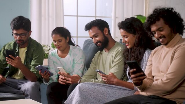 Group of Indian friends busy using or addicted to smartphones during home gathering - concept of mobile phone distraction, cyberspace and social media sharing