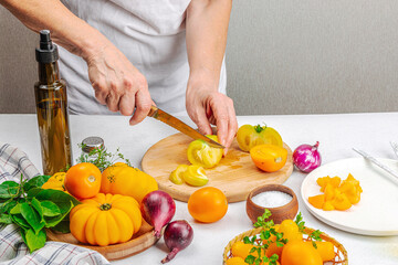 A woman is preparing a tomato salad. Ripe vegetables, herbs, aromatic spices, olive oil