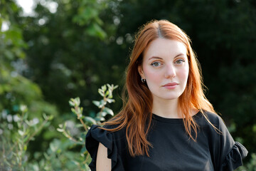 Fototapeta premium Candid ginger woman looking at camera in the green park. Calm and Relaxed