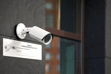Primo piano di una telecamera di videosorveglianza sul muro di un edificio con cartello bianco...