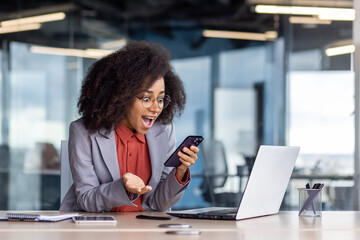 Excited young businesswoman with curly hair rejoices at her success while working in a contemporary...