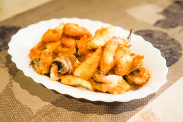 Fried cuttlefish on a white plate with a textured backdrop.