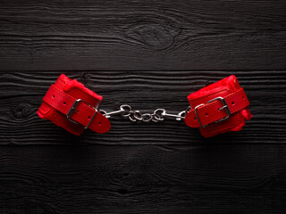 BDSM role play background with bright red handcuffs over black wooden backdrop
