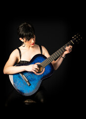 Obraz premium A young, beautiful woman in black with an acoustic blue guitar
