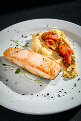 Close-up of salmon steak with hummus and tomatoes on a white plate