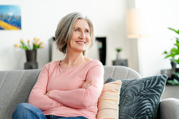 Happy confident senior woman holding arms crossed sitting on comfortable sofa at home. Portrait...