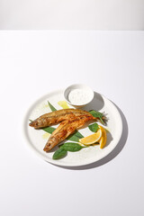 Grilled vendace fish with lemon and sour cream on a white plate, ideal for culinary presentations and food marketing