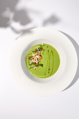 Top view of spinach cream soup with squid garnished with herbs, casting a soft shadow on white, ideal for modern cuisine publications