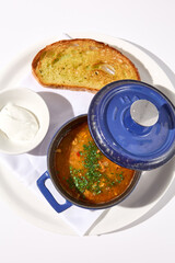 Top view of aromatic fish soup with a smoky touch, served in a cobalt blue pot with croutons and sour cream, isolated on white