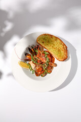 Sautéed shellfish in tomato sauce with garlic ciabatta toast, top view on white with dramatic...