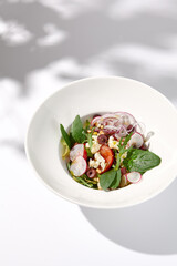 Greek salad with feta cheese, olives, and crisp vegetables, cast with shadows on a white background